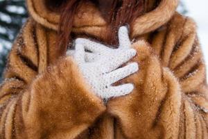 les mains de la femme dans des gants tricotés blancs se bouchent. femme en manteau de fausse fourrure avec des flocons de neige. photo