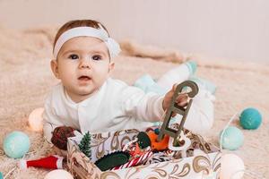 jolie petite fille en robe bleue et blanche joue avec des décorations de noël et des lumières de noël sur un plaid beige. photo