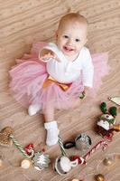 petite fille souriante en blouse blanche et jupe en mousseline rose joue avec des décorations de noël sur un plaid tricoté beige. photo