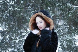 jeune belle femme souriante aux yeux bleus en manteau de fausse fourrure noire avec capuche rouge sur fond de parc enneigé d'hiver. photo