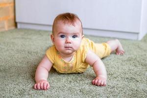 portrait de petite fille caucasienne en robe jaune. enfant essayant de ramper sur un sol. photo