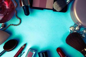 cadre d'un ensemble de cosmétiques féminins d'un rouge à lèvres, d'un surligneur, d'un crayon pour les lèvres, pinceaux, pinceaux, parfum, poudre, ornements sur fond bleu. boîte de beauté mise à plat. vue de dessus photo