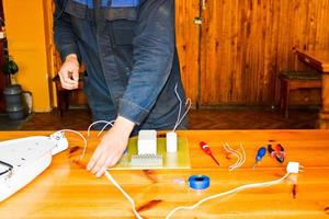 un homme travaillant électricien travaille, recueille le circuit électrique d'un grand réverbère blanc avec des fils, un relais dans une usine industrielle photo