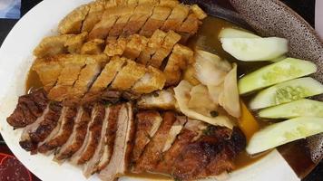 gros plan de canard grillé et de porc croustillant avec des tranches de concombre frais et du gingembre mariné dans une sauce à la sauce sucrée sur une assiette blanche ou un plat au restaurant chinois. nourriture asiatique. photo