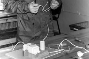 un homme travaillant électricien travaille, recueille le circuit électrique d'un grand réverbère blanc avec des fils, un relais dans une usine industrielle photo