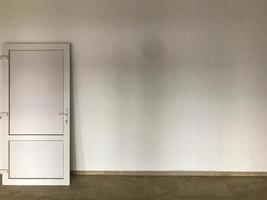 une porte en plastique blanc se dresse sur un mur en plâtre blanc. rénovation intérieure. installation de portes, décoration extérieure et intérieure. réparer une porte sur un sol peint en marron photo