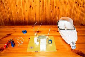 un grand réverbère blanc démonté avec un circuit électrique avec des fils et des pièces de rechange, du matériel d'installation, des pinces, du ruban électrique bleu, des tournevis sur la table photo