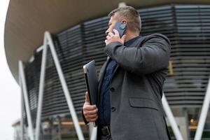 homme d'affaires masculin parlant sur un téléphone portable dans le contexte d'un immeuble de bureaux, concept d'un agent immobilier prospère photo