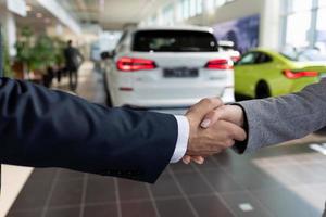 Acheteur et vendeur chez un concessionnaire automobile se serrant la main après avoir acheté une voiture photo