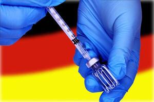 les mains en gros plan dans des gants médicaux bleus tirent un vaccin d'un flacon dans une seringue sur le fond du drapeau de l'allemagne. concept de grève des médecins. photo