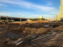 chantier de construction avec du sable et de l'eau. des ordures, des matériaux de construction, des flaques de boue se trouvent à proximité. des matériaux de construction et des pièces de rechange se trouvent à côté du pont. construction d'un nouveau quartier photo