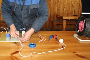 un homme travaillant électricien travaille, recueille le circuit électrique d'un grand réverbère blanc avec des fils, un relais dans une usine industrielle photo