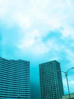 un immeuble d'appartements haut et lumineux au centre-ville. immeuble résidentiel de grande hauteur en blanc contre un ciel bleu clair. près d'une maison bleue en forme de vague. nouveau quartier de la ville photo