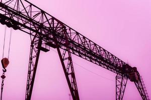 grande grue à portique métallique en fer industriel avec un crochet monté sur les supports pour soulever et transporter des charges lourdes, se déplaçant le long des rails à l'usine. la grue est de type pont photo