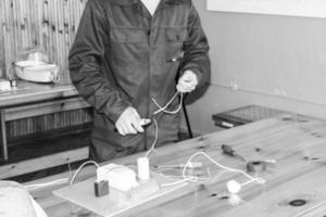 un homme travaillant électricien travaille, recueille le circuit électrique d'un grand réverbère blanc avec des fils, un relais dans une usine industrielle photo