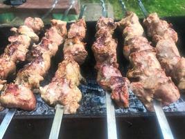 de belles viandes savoureuses et appétissantes, des brochettes grillées sur des charbons et de la fumée naturelle sur le gril avec une croûte fumée rôtie sur des brochettes. concept camping, pique-nique, barbecue, grillade photo