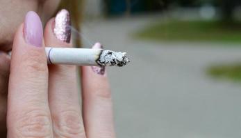 fille avec une manucure violette serre une cigarette photo