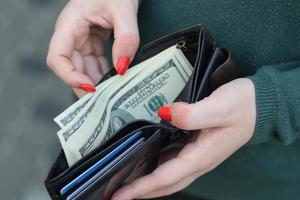 les mains de femme avec des ongles rouges tiennent un sac à main pour homme noir avec de nombreux billets de cent dollars américains. concept de salaire ou de compter l'argent photo