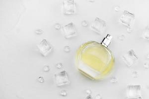 bouteille jaune de parfum féminin, photographie objective de la bouteille de parfum dans des glaçons et de l'eau sur un tableau blanc. vue d'en-haut. photo de produit maquette, concept de fraîcheur