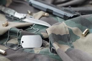 Jeton d'étiquette de chien de l'armée avec des balles de 9 mm et un pistolet allongé sur un tissu vert camouflage plié photo