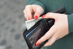 les mains de femme avec des ongles rouges tiennent un sac à main pour homme noir avec de nombreux billets de cent dollars américains. concept de salaire ou de compter l'argent photo