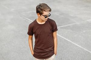 jeune homme élégant avec une coiffure et des lunettes de soleil sur fond gris. photo