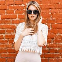 belle femme sexy élégante dans un chemisier en dentelle vintage blanc et des lunettes de soleil posant près du mur de briques rouges photo