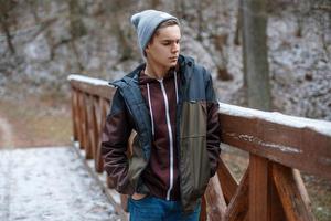 jeune bel homme se tient sur un pont en bois sur le fond de la forêt d'hiver photo