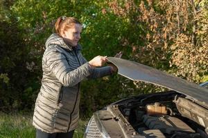 une femme en veste essaie de réparer une voiture cassée sur la route. photo