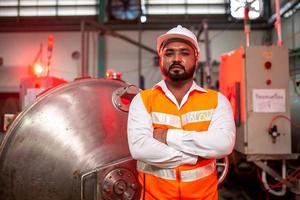 ingénieur professionnel avec casque travaille pour entretenir l'équipement de construction industrielle. le travailleur est debout dans l'usine avec les bras croisés. photo