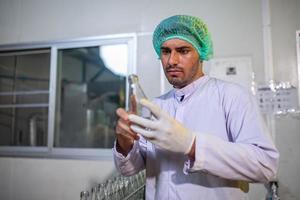 une travailleuse asiatique vérifie les bouteilles de jus de fruits sur la ligne de production de l'usine de boissons. le fabricant vérifie la qualité de l'industrie alimentaire. photo