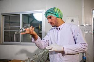 une travailleuse asiatique vérifie les bouteilles de jus de fruits sur la ligne de production de l'usine de boissons. le fabricant vérifie la qualité de l'industrie alimentaire. photo
