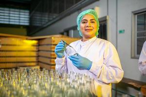 les travailleurs asiatiques avec presse-papiers vérifient les bouteilles de jus de fruits sur la ligne de production de l'usine de boissons. le fabricant vérifie la qualité de l'industrie alimentaire. photo