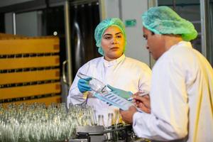 les travailleurs asiatiques avec presse-papiers vérifient les bouteilles de jus de fruits sur la ligne de production de l'usine de boissons. le fabricant vérifie la qualité de l'industrie alimentaire. photo