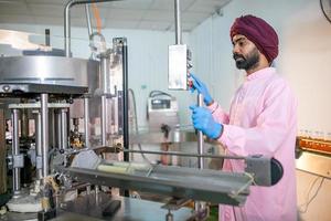 un travailleur asiatique avec presse-papiers vérifie les bouteilles de jus de fruits sur la ligne de production de l'usine de boissons. le fabricant vérifie la qualité de l'industrie alimentaire. photo