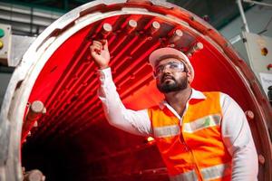 ingénieur technicien professionnel avec casque de sécurité travaillant à l'entretien des équipements de construction dans une usine industrielle, le travailleur vérifie ou répare la machine. photo