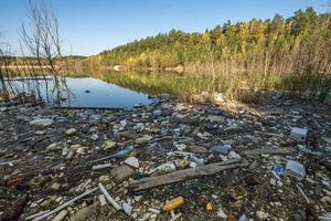 tas de déchets de construction, de déchets ménagers, de mousse et de bouteilles en plastique sur la rive d'un lac forestier, problèmes de pollution de l'environnement photo