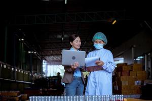 ouvrier scientifique dans une usine de boissons en bouteilles portant un chapeau de sécurité posant un travail de démonstration pour vérifier la qualité des produits de graines de basilic sur le tapis roulant avant la distribution aux entreprises du marché. photo