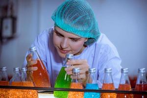 ouvrier scientifique dans une usine de boissons en bouteilles portant un chapeau de sécurité posant un travail de démonstration pour vérifier la qualité des produits de graines de basilic sur le tapis roulant avant la distribution aux entreprises du marché. photo