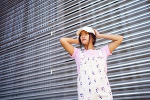 faible angle de femme asiatique heureuse dans des vêtements décontractés, portant une casquette, debout près d'un bâtiment moderne. photo