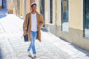 jeune homme noir marchant dans la rue portant une mallette et un smartphone. photo