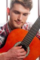 j'aime improviser. beau jeune homme jouant de la guitare acoustique et gardant les yeux fermés photo