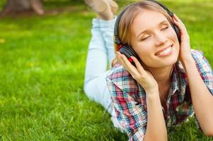 écouter de la musique préférée dans la nature. belle jeune femme au casque écoutant de la musique et souriant en position allongée sur l'herbe verte photo