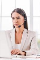 soutenir votre entreprise. belle jeune femme d'affaires dans un casque à l'aide d'un ordinateur alors qu'elle était assise sur son lieu de travail photo