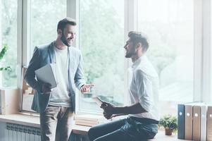 discuter de leur projet réussi. deux jeunes hommes d'affaires en vêtements décontractés intelligents parlant et faisant des gestes tout en se penchant sur le rebord de la fenêtre au bureau photo