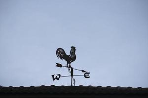 l'ancienne girouette avec une icône de symbole de coq sur le toit, équipement technologique traditionnel pour prévoir et mesurer le temps venteux dans l'air, décoration vintage, instrument de direction du vent visant. photo