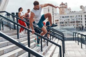 jeune homme en vêtements de sport sautant tout en faisant de l'exercice avec ses amis dans les escaliers à l'extérieur