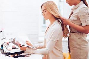 vie de mannequin. vue latérale d'une belle jeune femme lisant un magazine pendant que la coiffeuse ajustait ses cheveux dans la salle de maquillage photo