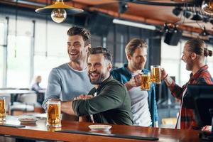 acclamant les jeunes hommes en tenue décontractée regardant un match de sport et dégustant une bière assis dans le pub photo