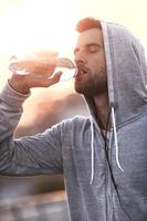 rester hydraté. jeune homme confiant buvant de l'eau tout en se tenant à l'extérieur photo